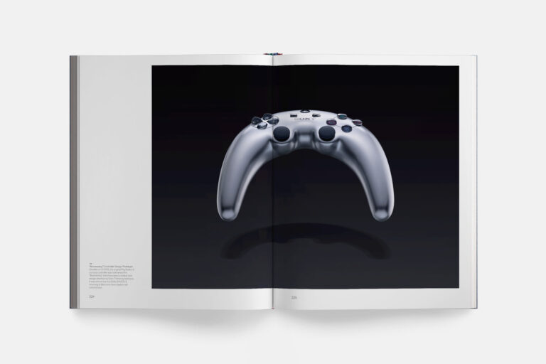 Libro PlayStation: The First 30 Years abierto por una fotografía del prototipo de mando bumerán de PS3