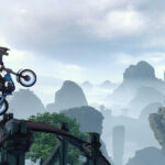 Un motorista de Trials Rising salta sobre unas rocas con montañas al fondo
