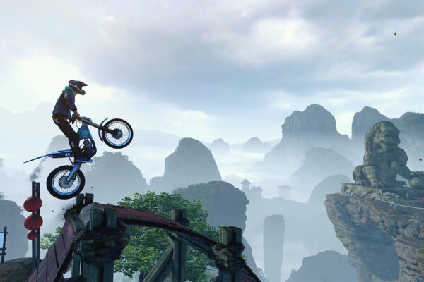 Un motorista de Trials Rising salta sobre unas rocas con montañas al fondo